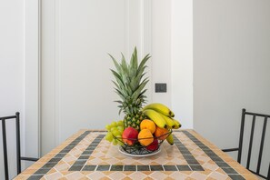 A dining table with a fruit bowl containing pineapple, bananas, grapes, and oranges.