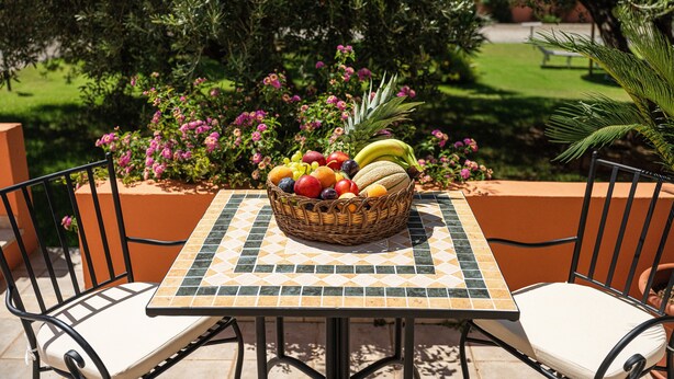 Une table d’extérieur avec un panier de fruits, deux chaises et un plateau de table recouvert de carreaux.