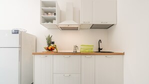 Une cuisine avec des meubles blancs, un plan de travail en bois, un évier et un panier de fruits.