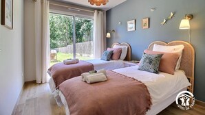 A bedroom with two beds, a large window, and a view of the garden.