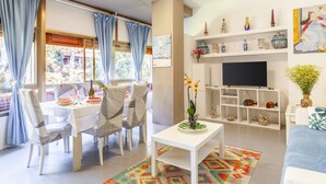 Een woonkamer met een eethoek, een televisie en planken met decoratieve objecten.