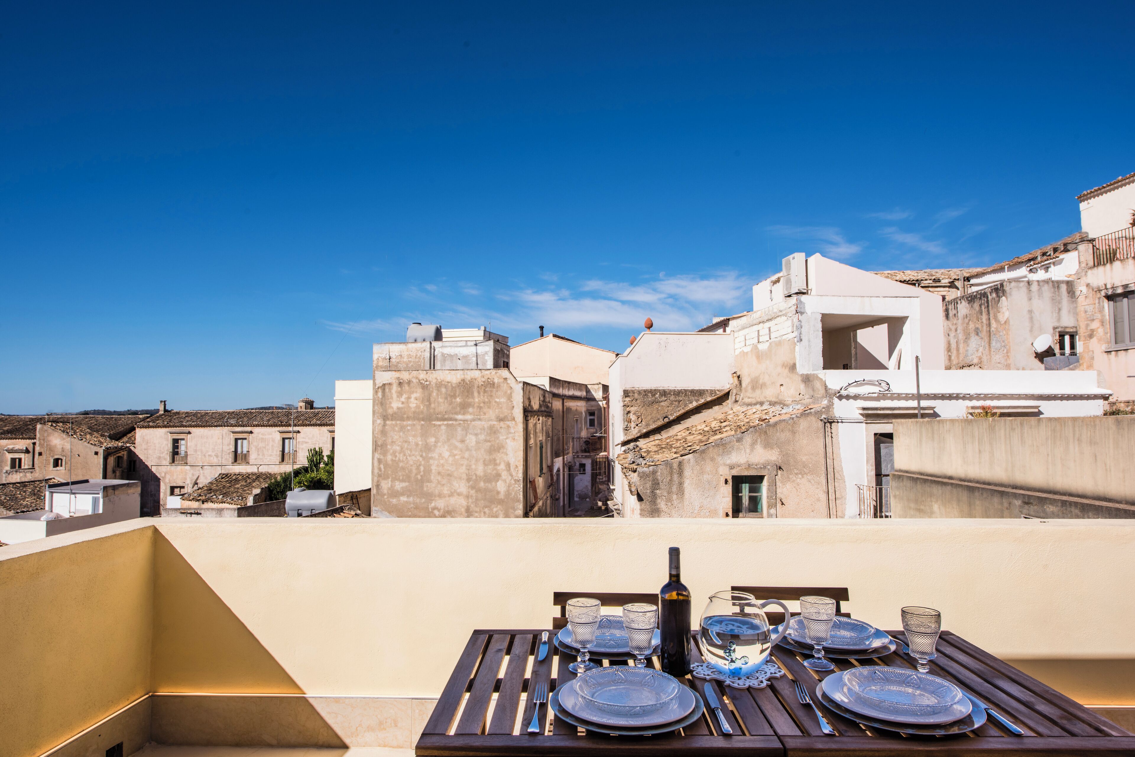 A rooftop terrace with a table set for dining, overlooking a historic town with traditional architecture.