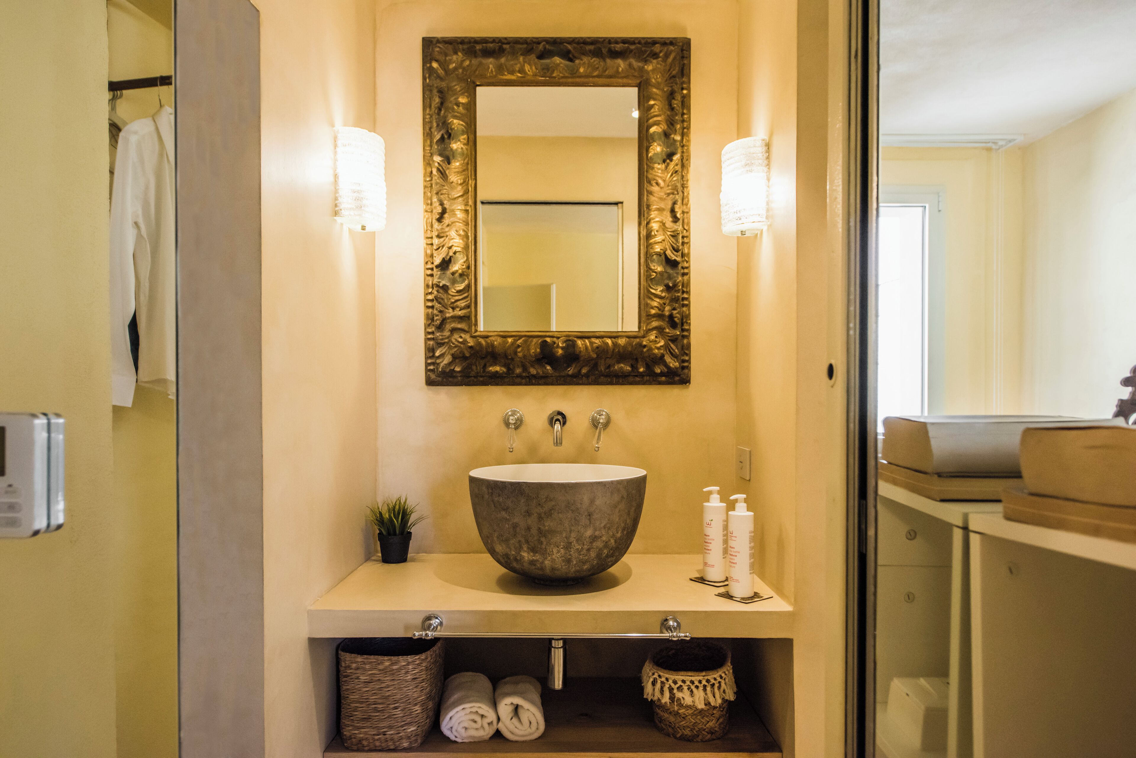 A bathroom with a large bowl sink, a mirror with an ornate frame, and two wall-mounted lights.