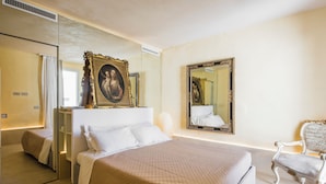 A modern hotel room with a large bed, a sitting area with a chair, and a mirror reflecting the room. - Casa Novella con Terrazza by Wonderful Italy (Noto)