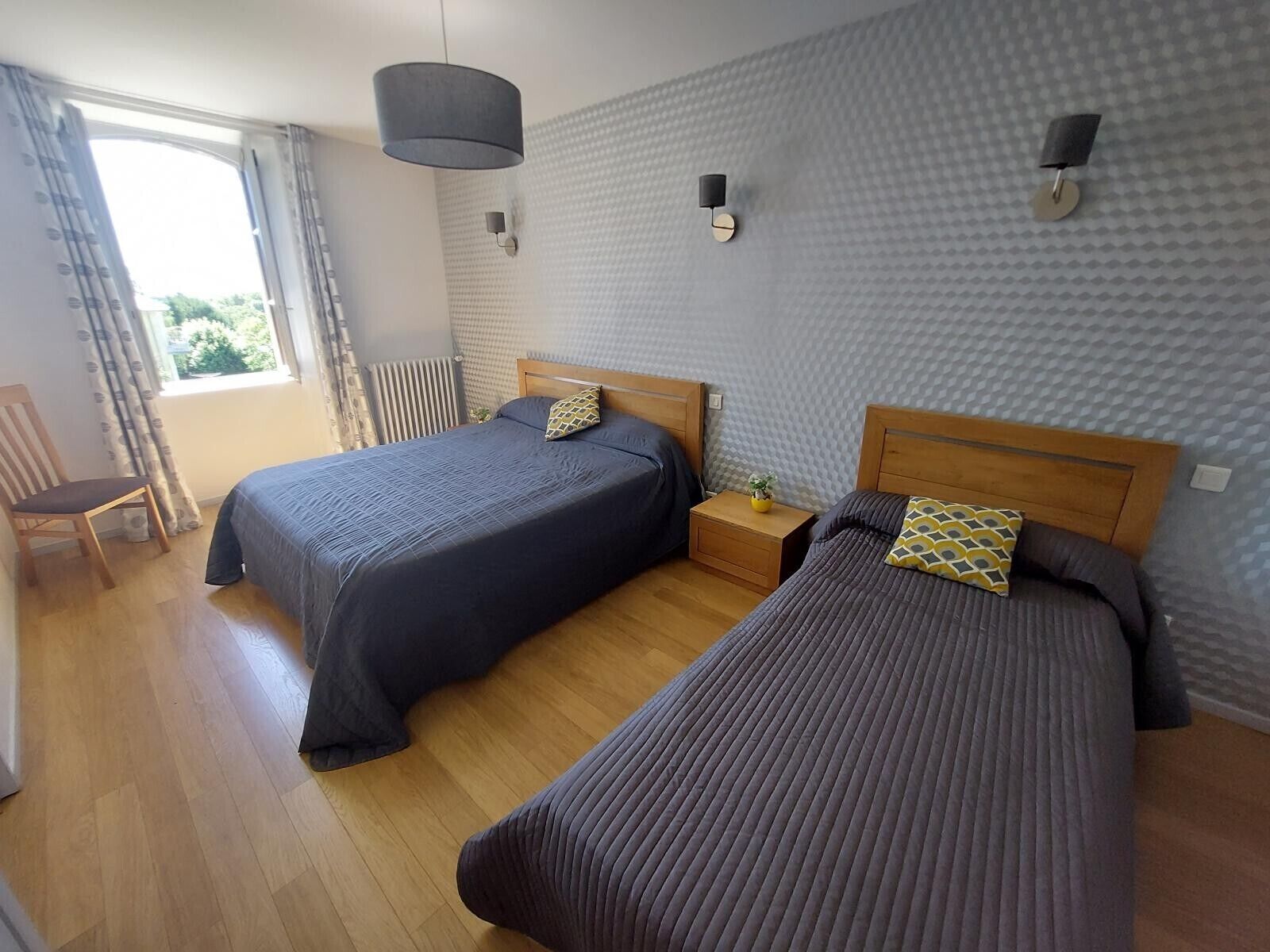 Habitación de hotel con dos camas, suelo de madera, ventana con cortinas y una lámpara en el techo.