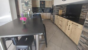 A modern kitchen with a central island, a dining table, and a large wall clock. - Holiday Home 'Gîte La Chartrouille' with Private Terrace, Private Garden and Wi-Fi (Allassac)