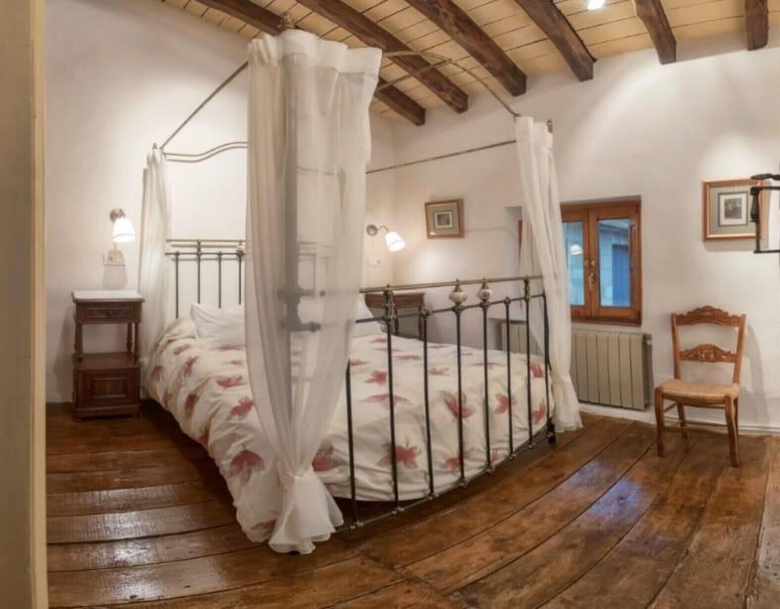Un dormitorio con cama de dos plazas, suelo de madera, una silla y una mesita de noche.