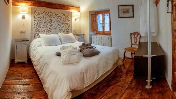 Een slaapkamer met houten vloer, een bed met wit beddengoed, een nachtkastje, een stoel en een radiator.