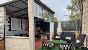 A covered outdoor area with a barbecue, seating, and a stone wall. - Casa La Molina – Spacious Countryside Home with Mountain Views near Burgos (Burgos)