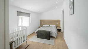 A bedroom with a bed, a nightstand, a window, a crib, a bench, and a framed picture on the wall. - Casa La Molina – Spacious Countryside Home with Mountain Views near Burgos (Burgos)