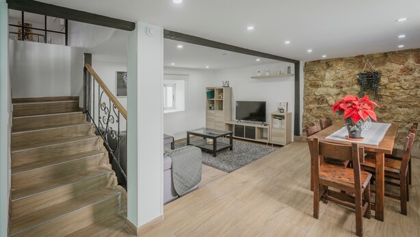 A spacious living area with a staircase, a dining table with chairs, a television, and a stone wall. - Casa La Molina – Spacious Countryside Home with Mountain Views near Burgos (Burgos)