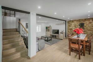 A spacious living area with a staircase, a dining table with chairs, a television, and a stone wall. - Casa La Molina – Spacious Countryside Home with Mountain Views near Burgos (Burgos)