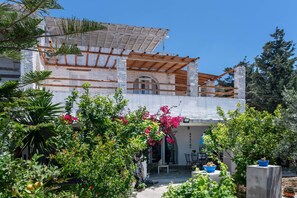 Ein Gebäude mit überdachter Terrasse, Säulen aus Stein und einem Garten mit verschiedenen Pflanzen und Blumen.