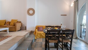 Sala de estar com sofá, mesa de jantar com cadeiras, uma mesinha lateral e um objeto decorativo na parede.