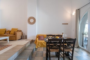 A living area with a sofa, a dining table with chairs, a small side table, and a decorative wall piece.