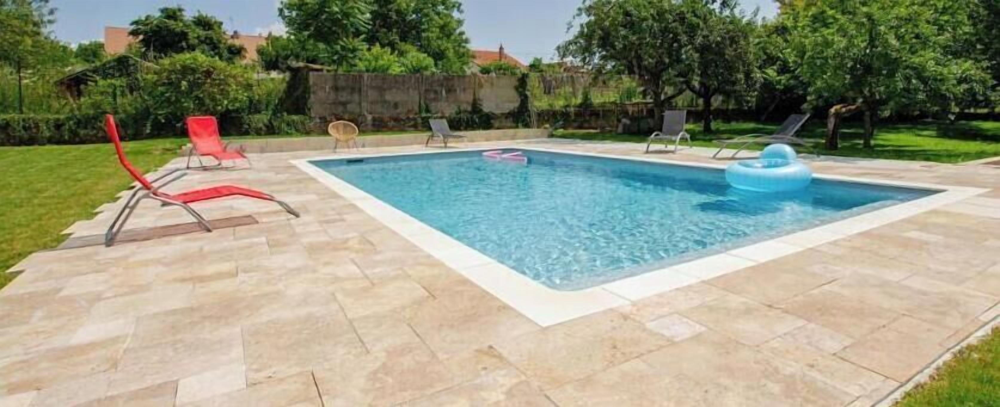 A rectangular swimming pool with a tiled deck, surrounded by lounge chairs and a grassy area.