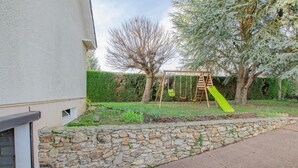 A stone wall, a swing set, and a green slide in a backyard. - Chez Alice - VILLENAUXE LA GRANDE (VILLENAUXE LA GRANDE)