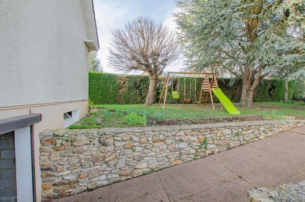 Un mur de pierres, une balançoire et un toboggan vert dans un jardin.
