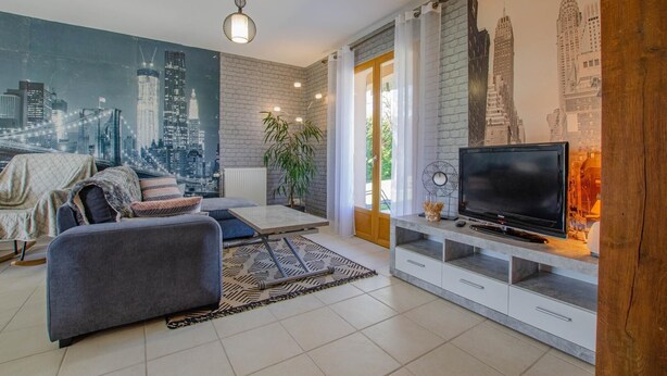 Ein modernes Wohnzimmer mit Stadtbild-Wandgemälde, einem grauen Sofa, einem Fernseher und einer Wandpaneele aus Holz.