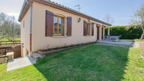 Einbungalow mit kleinem Vorgarten, einer Terrasse mit Gartenmöbeln und blauem Himmel.