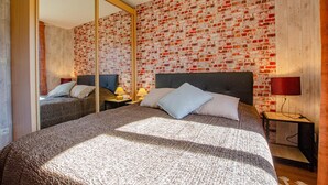 Ein Doppelbett mit strukturierter Bettdecke, zwei Nachttische mit Lampen und eine Wand mit Ziegeloptik.