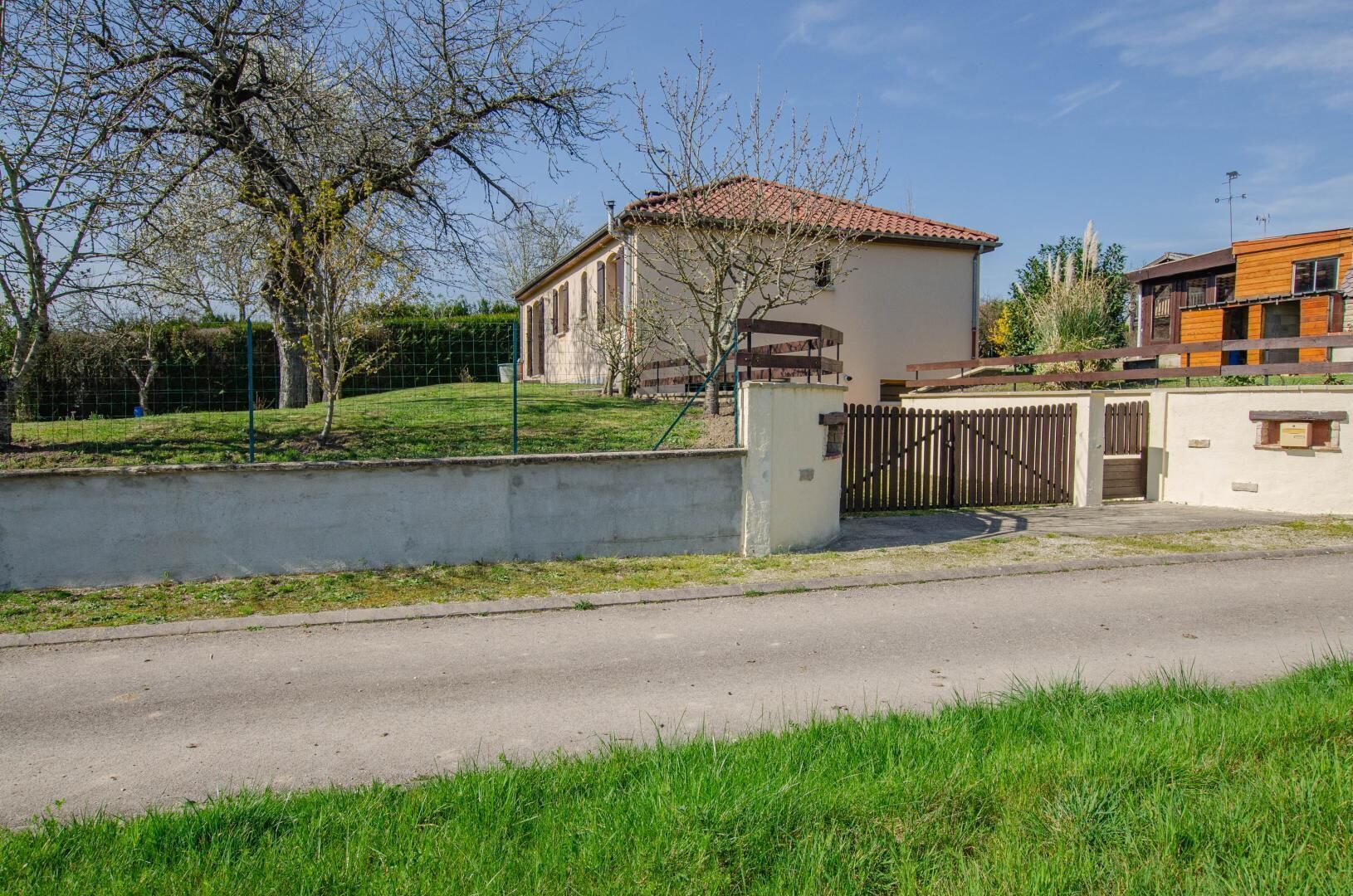 A residential area with a house featuring a tiled roof, a fenced yard, and a paved road in the foreground.