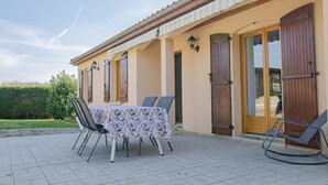 Eine Terrasse mit Tisch für zwei Personen, Sitzgelegenheit im Freien und ein Gebäude mit großen Holztüren und -fenstern.