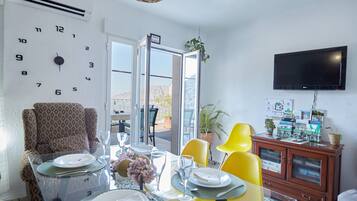 A dining area with a table set for four, a clock on the wall, and a television mounted above a cabinet.