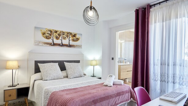 Une chambre d’hôtel avec un lit, des lampes de chevet, un bureau avec un ordinateur portable, un tableau au mur et une fenêtre avec des rideaux.