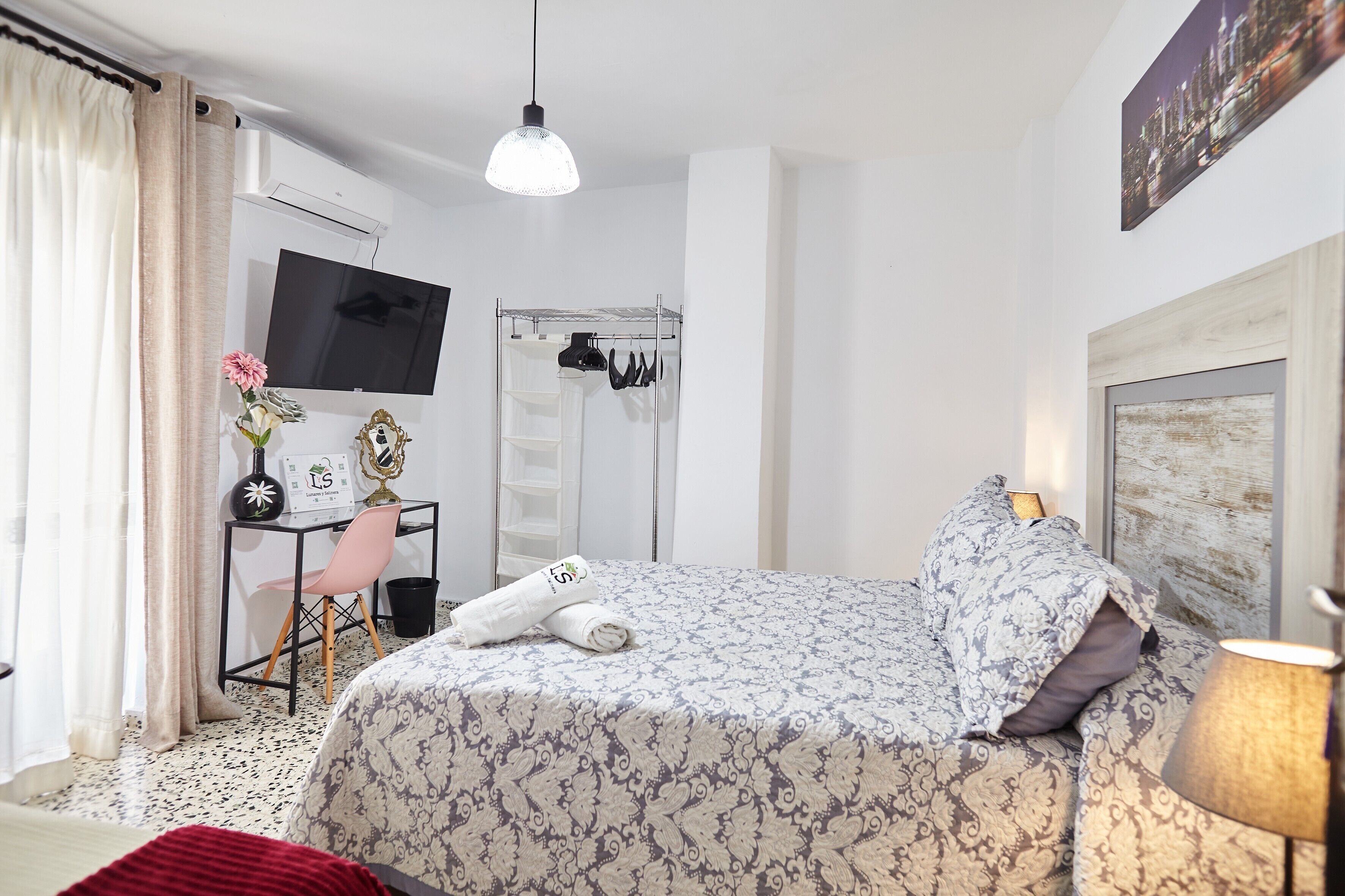 Un dormitorio con cama, escritorio con silla, televisor y zona de ducha.
