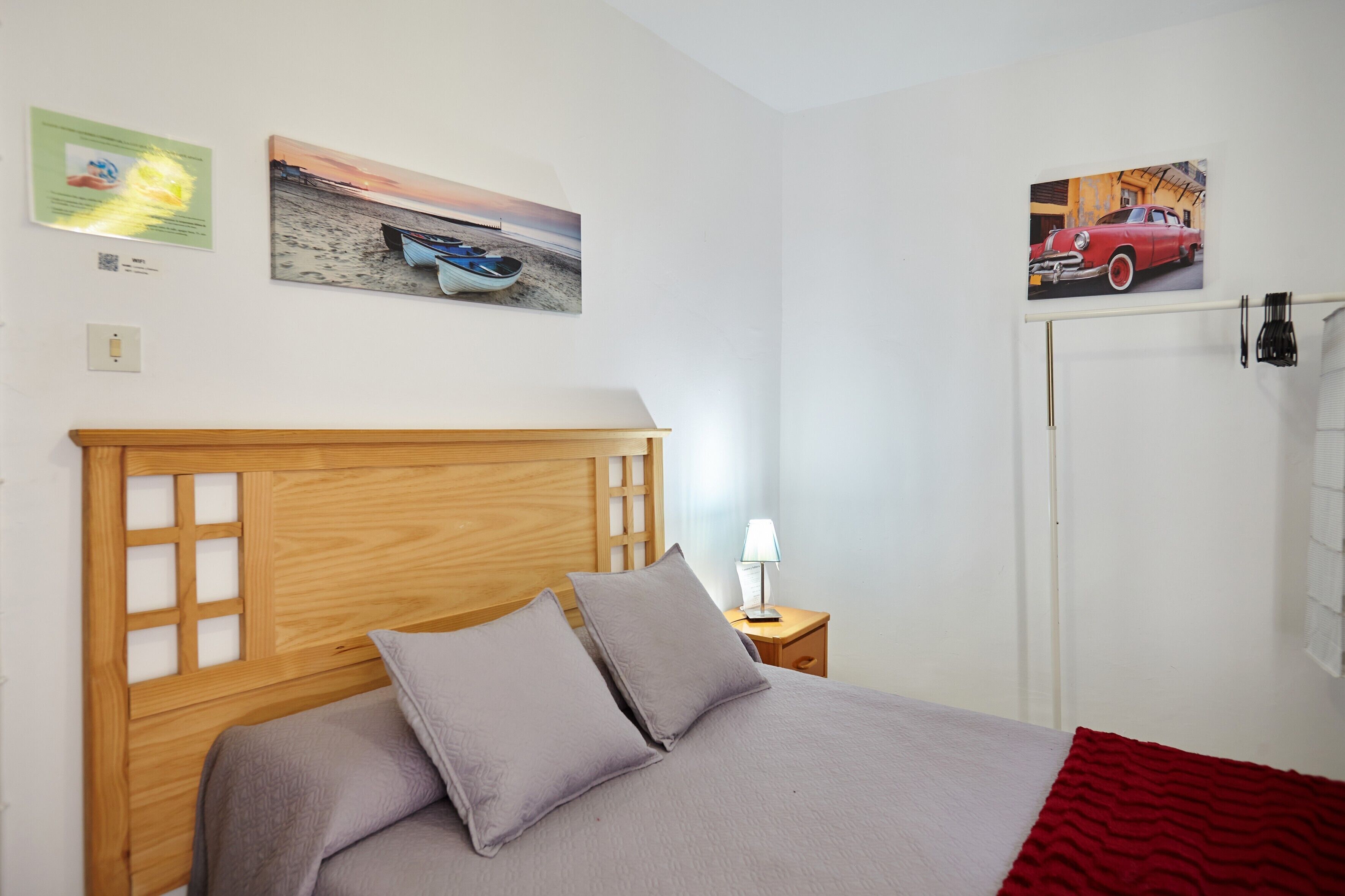 Un dormitorio con cabecera de madera, cama con ropa de cama gris, mesita de noche con lámpara y decoración en la pared que muestra un barco y un coche.