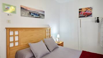 Un dormitorio con cabecera de madera, cama con ropa de cama gris, mesita de noche con lámpara y decoración en la pared que muestra un barco y un coche.