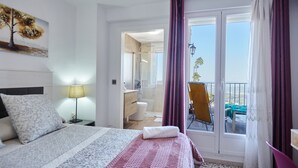 Une chambre d’hôtel comprenant un lit, une table de chevet, une lampe, une salle de bain et un balcon avec une chaise.