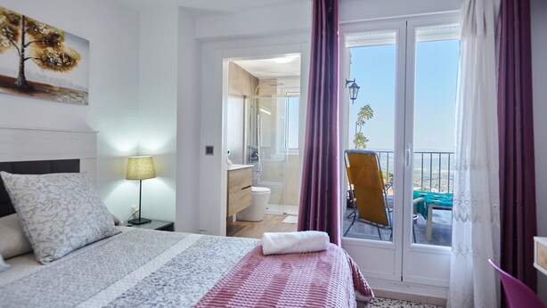 Ein Hotelzimmer mit Bett, Nachttisch, Lampe, Bad und Balkon mit Stuhl.