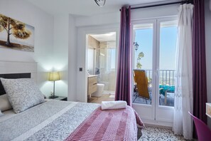 Une chambre d’hôtel comprenant un lit, une table de chevet, une lampe, une salle de bain et un balcon avec une chaise.