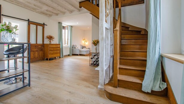 A spacious living area with a wooden staircase, a sofa, a coffee table, and a dining area with a chair and a table.