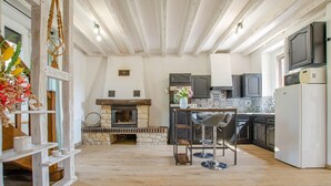 A cozy kitchen with a stone fireplace, wooden beams, and a bar area with stools.