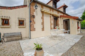 A building with a patio area featuring a stone floor, a bench, and a table with chairs.