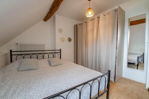 A bedroom with a sloped ceiling, a bed with a metal frame, a hanging light fixture, and a window with curtains.