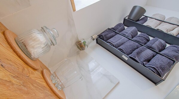A bathroom with a wooden vanity, a glass jar, a small glass bottle, and a towel rack with folded towels. - Le Gite de Saint Lyé (SAINT LYE)