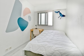 Een slaapkamer met een bed, een bureau, een stoel, een raam en wanddecoratie.