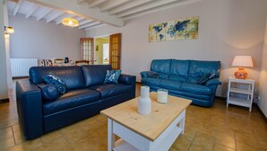 A living room with a blue leather sofa, a wooden coffee table, and a world map on the wall. - Le Marguette - PEPPERS (POIVRES)