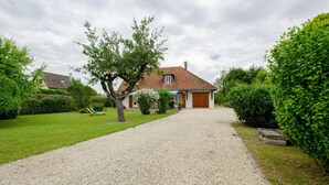 Une maison avec une allée en gravier menant à la porte d’entrée, entourée de pelouses et de haies bien entretenues.