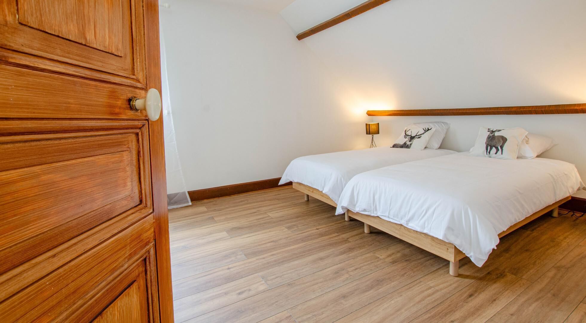 Un dormitorio con estructura de cama de madera, ropa de cama blanca y dos lámparas fijadas a la pared.