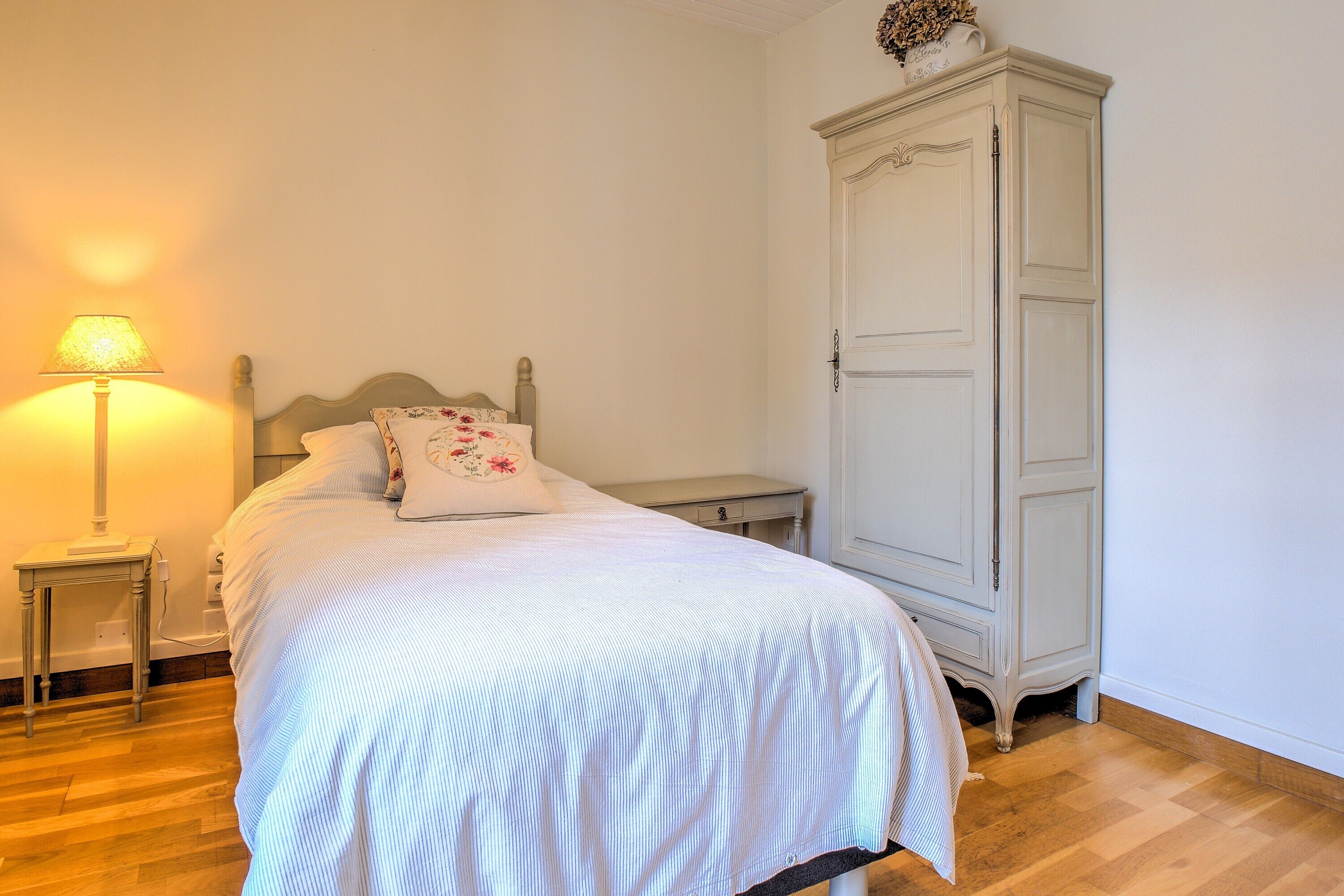 Quarto com cama, mesa de cabeceira, abajur e guarda-roupa.