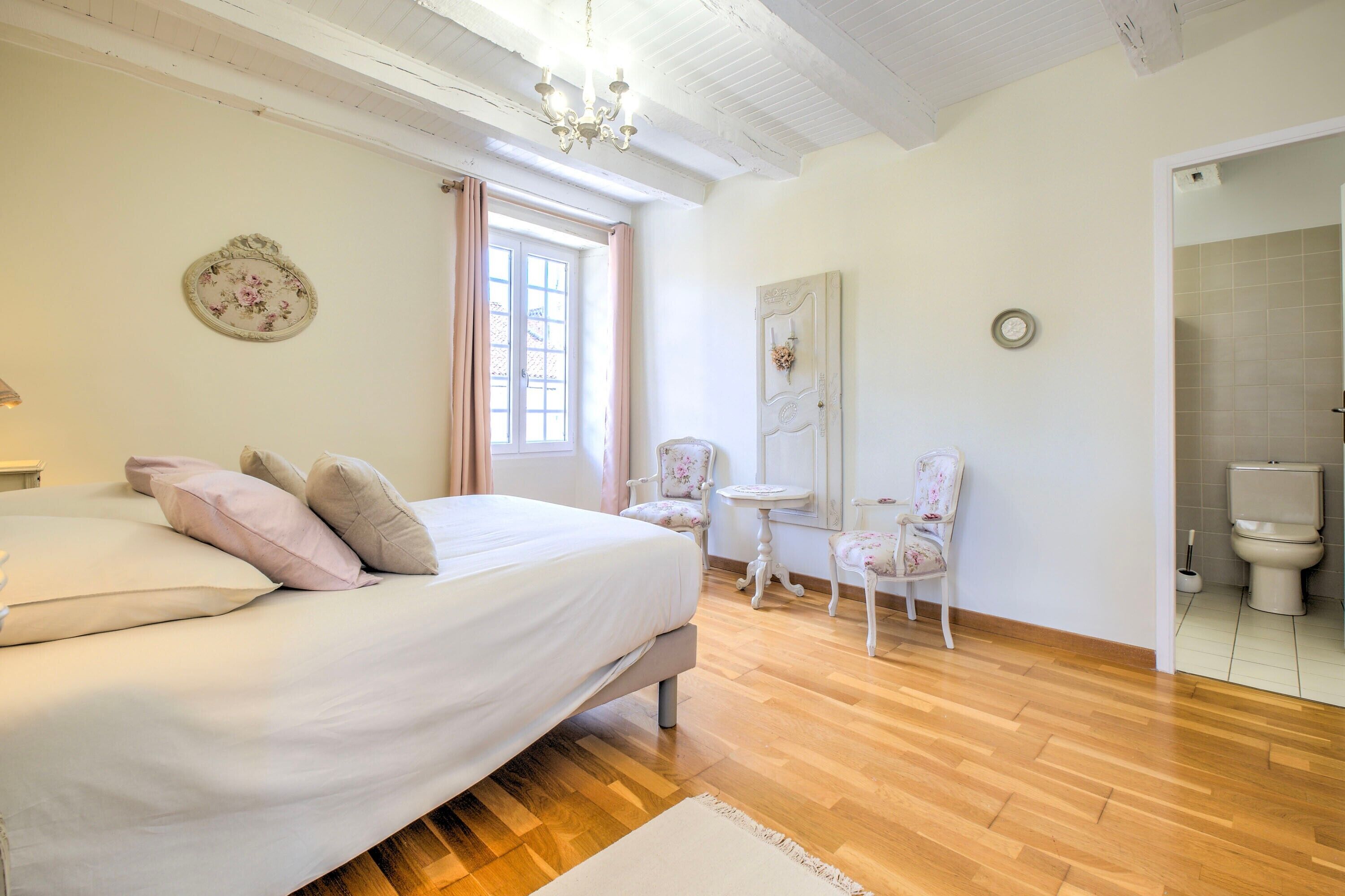 Une chambre à coucher comprenant un lit, une chaise, une table, une fenêtre et une porte donnant sur une salle de bain.