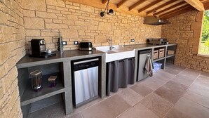 Una cocina con paredes de piedra y techo de madera, lavavajillas empotrado y un lavabo.