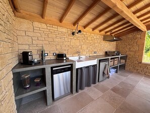 Une cuisine aux murs en pierre, avec un plafond en bois, un lave-vaisselle encastré et un évier.