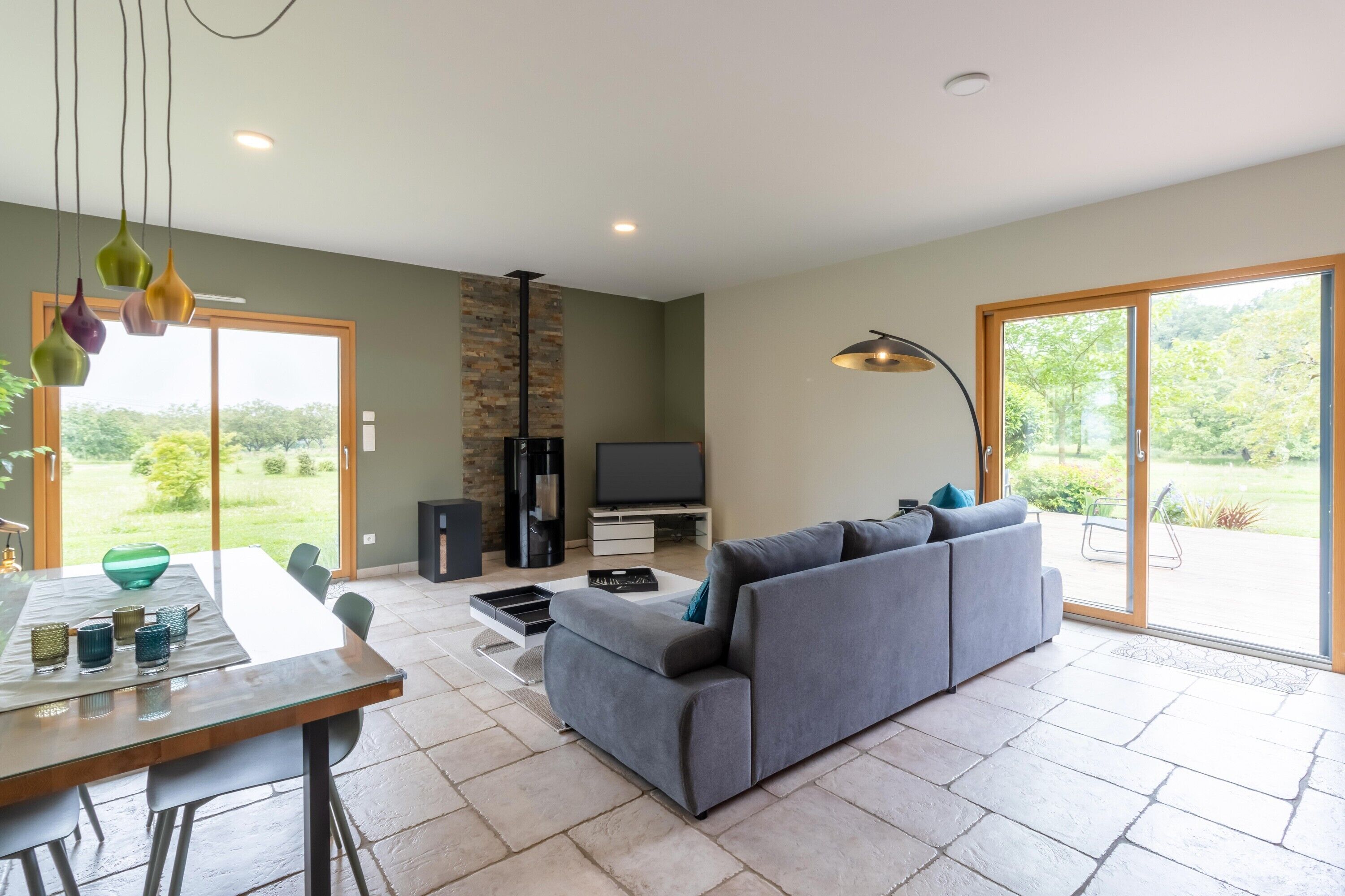 A modern living room with a grey sofa, a dining table with chairs, a TV, and a fireplace.
