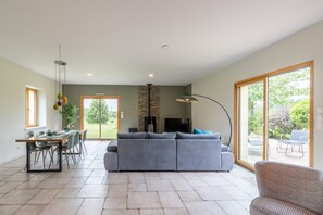 Amplia sala de estar con sofá, mesa de comedor y sillas, televisor y un gran ventanal corredizo que da a un patio exterior.